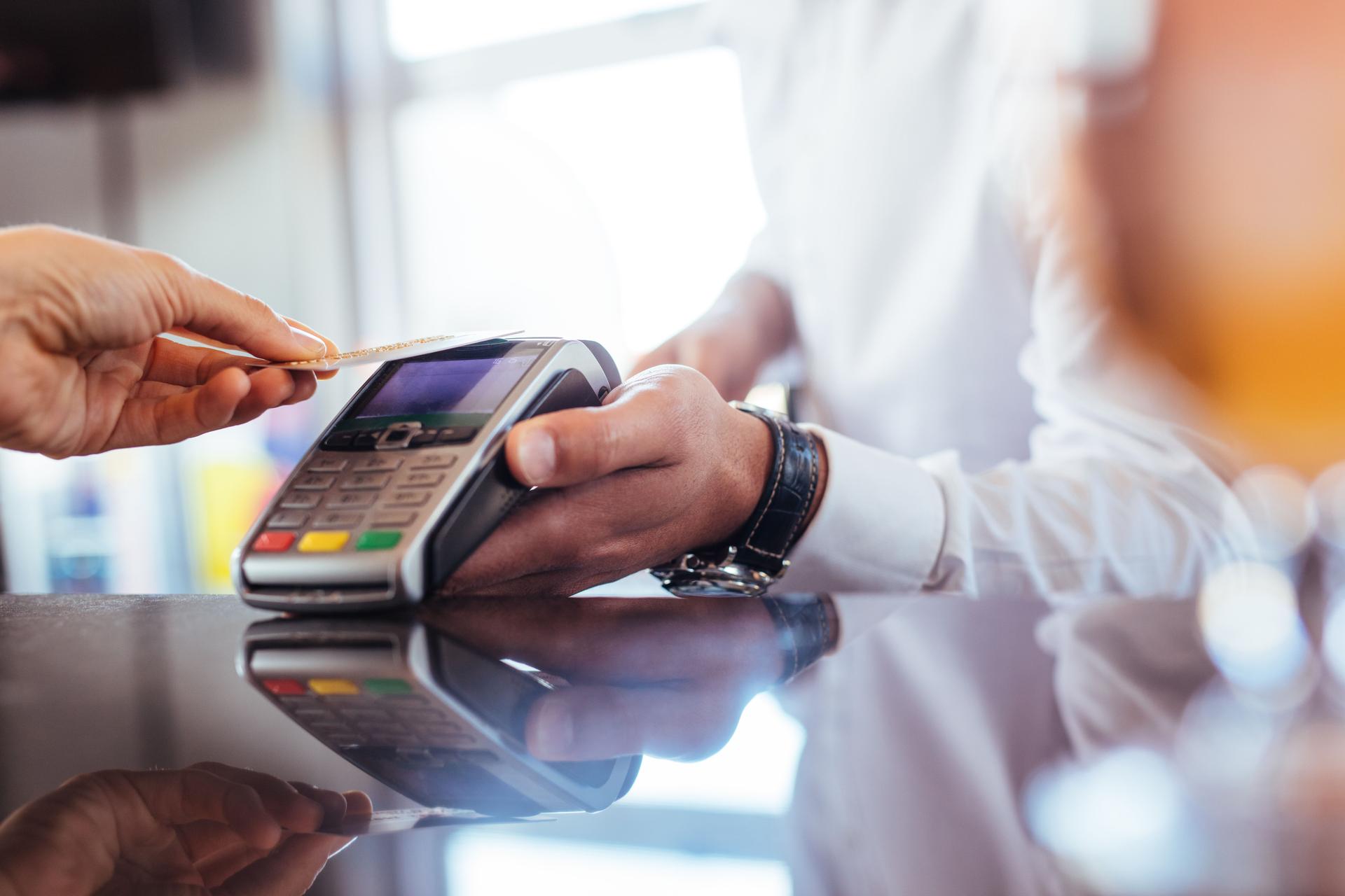 En person som betaler med kredittkort ved å holde et kredittkort mot en betalingsterminal.